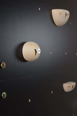 zbliżenie detalu czarnej ścianki wspinaczkowej Nuki i chwytów drewnianych do wspinaczki