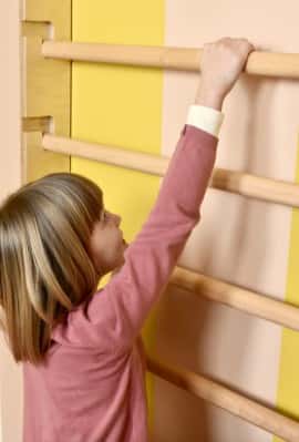 zbliżenie na dziecko wspinające się na drabinkę gimnastyczną Nuki FunActive  zamontowana na kolorowej ściany w pokoju dziecka