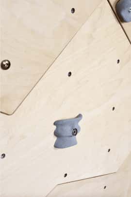 szary chwyt wspinaczkowy zamontowany na ściance wspinaczkowej w kolorze naturalne sklejki