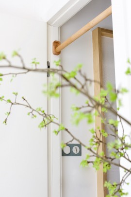 widok perspektywiczny na drewniany drążek do podciągania Nuki FunActive przez zielone gałęzie dekoracyjne